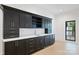 Elegant wet bar featuring dark cabinetry with gold hardware, light countertops, and open shelving at 7011 Chateau Bordeaux Ln, Charlotte, NC 28270