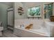 Bathroom with white tiled tub featuring caddy and shelf, and large window offering lush views at 110 Club Dr, Mooresville, NC 28115