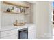 Chic wet bar with white cabinetry, floating shelves, marble countertops, tile backsplash, and beverage cooler at 811 Ashmeade Rd, Charlotte, NC 28211