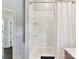 Bright bathroom with a shower-tub combo, featuring white subway tile and convenient glass shelving for storage at 19205 Hidden Cove Ln, Cornelius, NC 28031