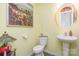 A well lit powder room with wood flooring features a round mirror and pedestal sink at 1220 Kent Downs Sw Ave, Concord, NC 28027