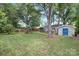 Spacious backyard featuring lush lawn, mature trees, a playset, and storage building with a blue geometric dome at 1744 Emerywood Dr, Charlotte, NC 28210