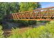 A metal truss pedestrian bridge spans over a muddy river surrounded by lush greenery at 240 Orson Oaks Ln, Pineville, NC 28134