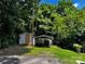 View of a backyard featuring a shed and a covered parking area surrounded by green grass and mature trees at 305 E Henry St, Belmont, NC 28012