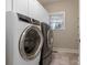 Well-lit laundry room featuring gray tile floors, modern washer and dryer, and white storage cabinets at 610 Hampshire Hill Rd, Matthews, NC 28105