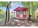 A cute red storage shed with a front porch, nestled among the trees at 16509 Kimbolten Dr, Huntersville, NC 28078