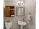 Charming powder room featuring a pedestal sink, wood storage cabinet, and decorative mirror at 911 Munday Ct, Charlotte, NC 28270