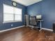 Home office with blue walls featuring a large window and a modern desk setup, with dark wood flooring at 9123 Magnolia Lily Ave, Charlotte, NC 28227