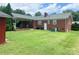 Back exterior with a brick facade, covered patio, lawn, and some trees at 1901 Taylor Dr, Gastonia, NC 28052