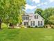 Charming white brick home featuring a lush green lawn, mature trees, and manicured landscaping at 1605 Ambergate Dr, Waxhaw, NC 28173