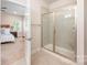 Bathroom with tile shower featuring clear glass enclosure and neutral-toned tile, next to primary bedroom at 7739 Village Pkwy, Locust, NC 28097