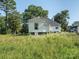 Backyard view of white house with grassy field with tall weeds and trees at 110 College St, Marshville, NC 28103