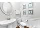 Elegant powder room with a pedestal sink, decorative mirror, and classic wall paneling at 10320 Lemington Dr, Mint Hill, NC 28227
