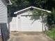 Exterior shot of a detached garage with a white door and siding, partially obscured by greenery at 6708 Nutcracker Pl, Charlotte, NC 28212