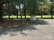 View of a light-colored shed with a grey roof, surrounded by trees, and standing on a gravel and dirt patch at 13221 Brandywine Ln, Midland, NC 28107