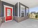 Inviting covered porch with a vibrant red front door, brick accents, and ample natural light at 1516 Respect Nw St, Concord, NC 28027