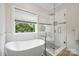 Modern bathroom with a freestanding tub, glass-enclosed shower, and a large window offering natural light and greenery views at 20444 Greenway Heights Dr, Cornelius, NC 28031