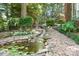 Landscaped backyard stream with river rock flowing between lush greenery and natural stone features at 2704 Apache Trl, Denver, NC 28037
