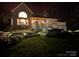 Charming home exterior with a well-lit deck, large windows, and beautifully landscaped yard at nighttime at 2704 Apache Trl, Denver, NC 28037