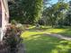 Lush backyard with green lawn, a stone landscaping element, a brick walkway and vibrant roses along the side of the house at 44112 Harper Hearne Rd, New London, NC 28127