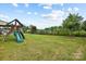Spacious backyard featuring a playset, green grass, and privacy fence with view of a wooded area at 7058 Cloer Ct, Charlotte, NC 28214