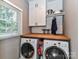 Bright laundry room with modern appliances, wooden countertop, white cabinets, and stylish shelving with metal accents at 3401 Cresta Ct, Charlotte, NC 28269