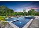 An elegant backyard swimming pool with a built-in spa, beautiful landscaping, and fire bowls at dusk at 1430 Rosehill Dr, Waxhaw, NC 28173