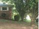 Backyard view with mature shade trees and partial view of brick home with white shutters at 1628 Cecelia Dr, Gastonia, NC 28054