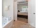En-suite bath with soaking tub and view into bedroom with a ceiling fan and window at 13510 Brandon Trail Dr, Charlotte, NC 28213