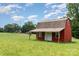 Charming red barn-style shed featuring a covered porch, set against a backdrop of open land at 544 Hicks Creek Rd, Troutman, NC 28166