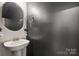 Stylish powder room with a pedestal sink, modern mirror, and sleek, dark accent wall at 13323 Savaine St, Charlotte, NC 28278