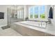 Bright bathroom featuring a soaking tub, tiled shower, and large window with plantation shutters at 200 Squash Harvest Ct, Matthews, NC 28104
