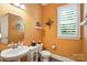 Charming powder room with orange walls, window with plantation shutters and pedestal sink at 200 Squash Harvest Ct, Matthews, NC 28104