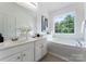 Bright bathroom with a dual sink vanity, large soaking tub under a window, and tiled floor at 10094 Treeside Ln, Matthews, NC 28105