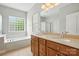 Bright bathroom featuring a double sink vanity, soaking tub, and glass block window for natural light at 10818 Alvarado Way, Charlotte, NC 28277