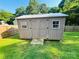 A backyard storage shed with a metal roof, double doors, and windows in a fenced yard with a grassy lawn on a sunny day at 1723 Lowder St, Albemarle, NC 28001