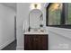 A modern bathroom featuring a wooden vanity with brass fixtures, an arched mirror, and a natural light window at 4209 Windwood Cir, Charlotte, NC 28226