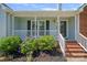 Inviting front porch with brick steps, white railing, black shutters, and lush landscaping with purple flowers at 142 Family Ln, Mount Holly, NC 28120
