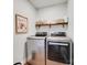 Bright laundry room with stainless steel washer and dryer and open wooden shelf with storage and decor at 2103 Cantata Ct, Matthews, NC 28105