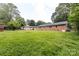 A large, grassy backyard features mature trees and the rear of the brick home at 6421 Hidden Forest Dr, Charlotte, NC 28213