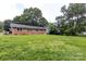A large, grassy backyard features mature trees and the rear of the brick home at 6421 Hidden Forest Dr, Charlotte, NC 28213