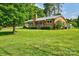 Well-maintained home with mature trees, lush lawn, and a welcoming red door at 7753 Caswell Rd, Stanley, NC 28164