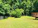 View of the grassy backyard with partial view of a wooden deck bordered by mature trees at 125 Circle Dr, Mount Holly, NC 28120