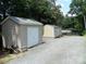 Backyard features two large sheds on a gravel lot next to the house and surrounding trees at 257 Rolling View Dr, New London, NC 28127