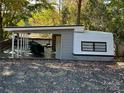 View of the charming exterior with a covered deck, white and gray finishes, and mature trees in the background at 112 Sycamore St, New London, NC 28127