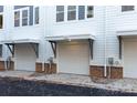 An exterior view shows the garages of the townhomes, with white doors, brick bottoms, and white siding at 1409 Collier Walk Aly # Csw0104, Charlotte, NC 28205