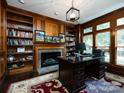 Home office with built-in bookshelves, a fireplace, and a large desk at 4409 Solemn Point Ln, Charlotte, NC 28216