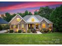 Twilight view of the home showcasing its brick and stone facade, landscaped yard, and warm interior lighting at 160 Northington Woods Dr, Mooresville, NC 28117