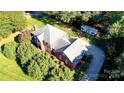 Aerial view of the red brick house with a large roof, well-maintained landscaping, and a long driveway at 102 Sleaford Ct, Dallas, NC 28034