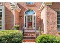 Elegant brick home entrance featuring an arched window over the doorway and manicured shrubbery at 15909 Woodcote Dr, Huntersville, NC 28078